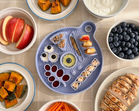 Assorted food items on the Smorgasbord Lick Mat from Awoo including fruits, vegetables, and meats on a table.